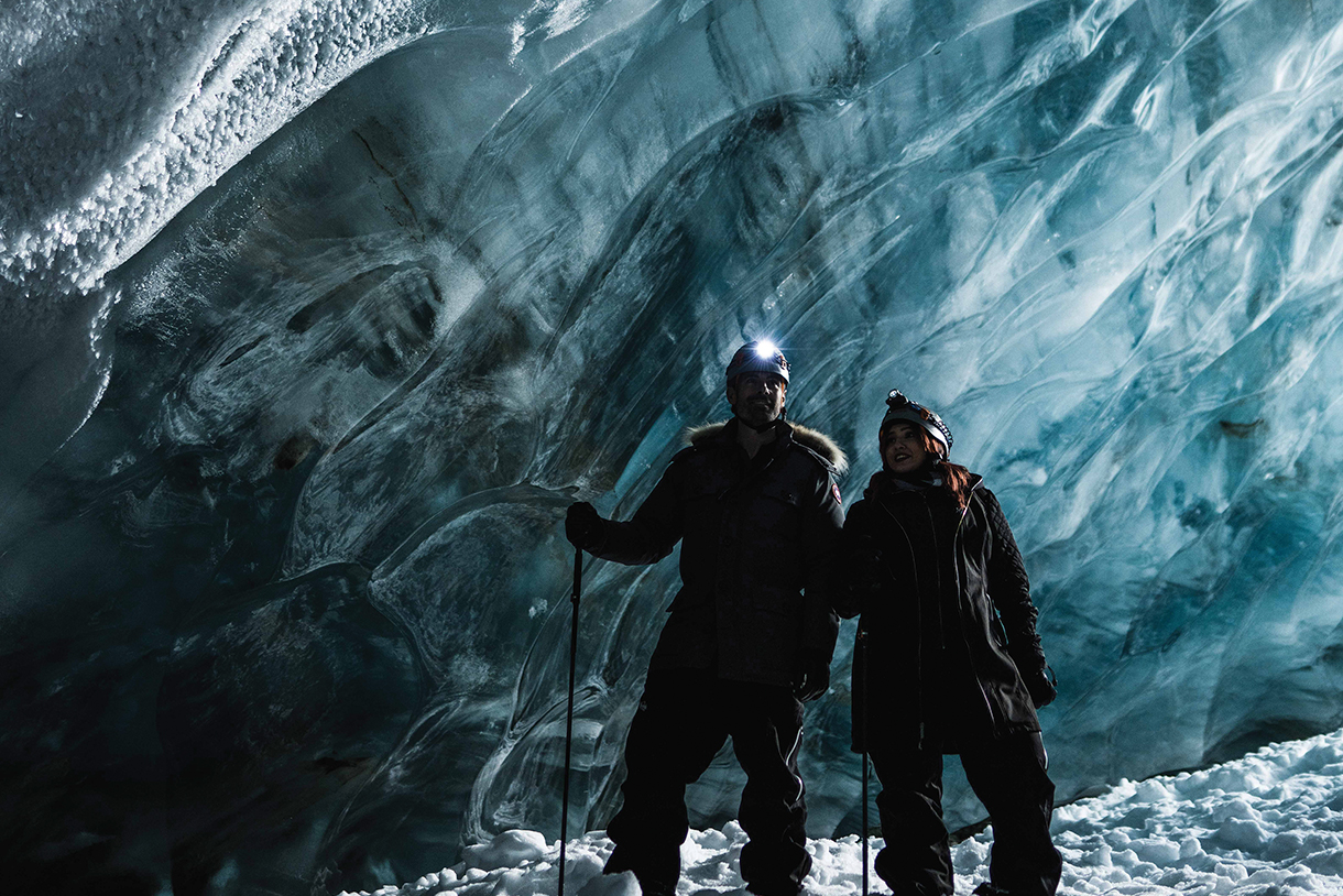 Two people wearing snow gear in a dark ice cave